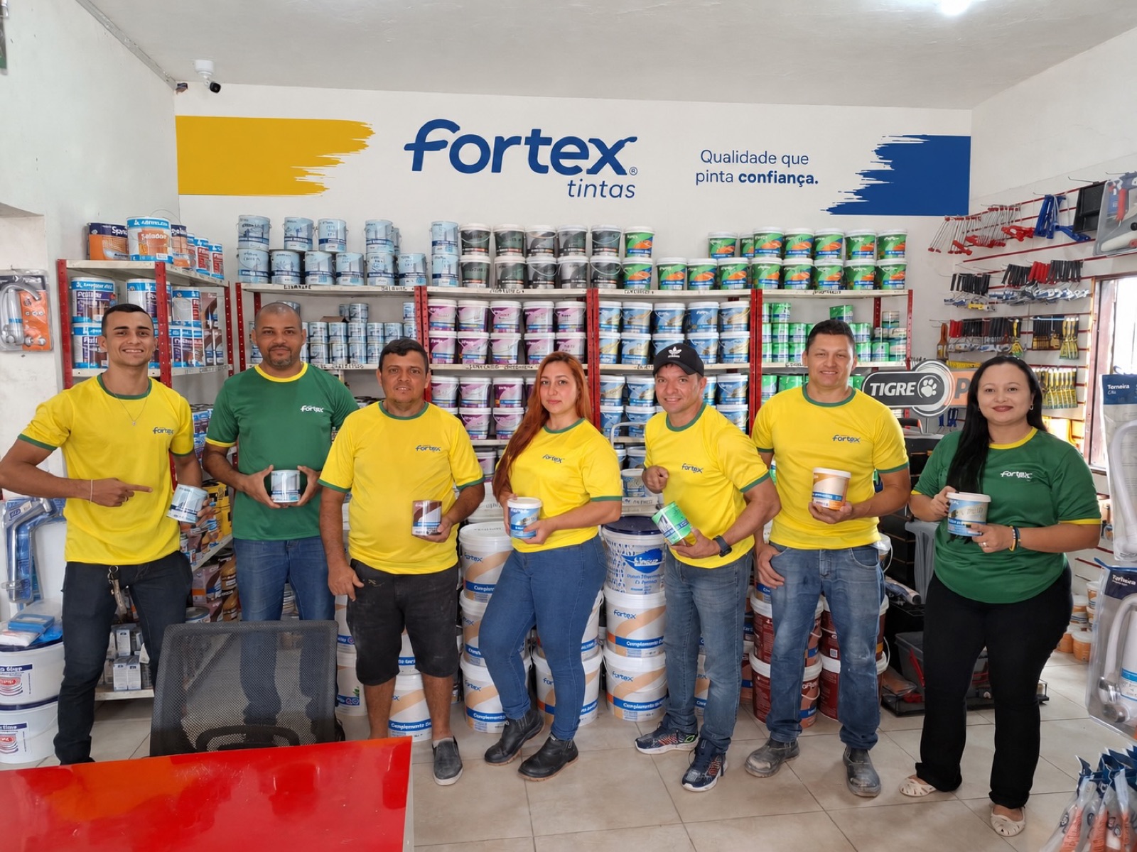 Equipe da Casa Soares no salão da loja, diante das prateleiras de latas de tinta e do painel de ferramentas.